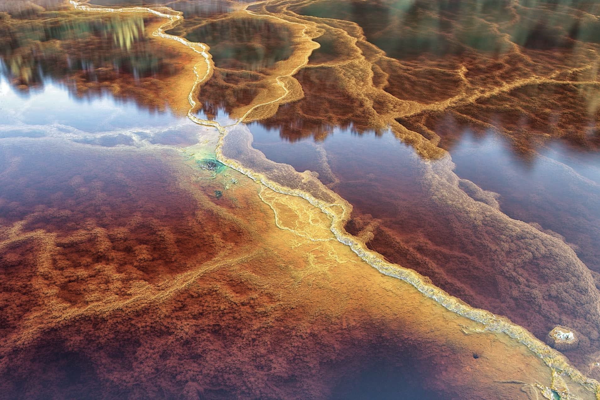 Aerial view of mineral-stained river water, streaked red, orange and yellow